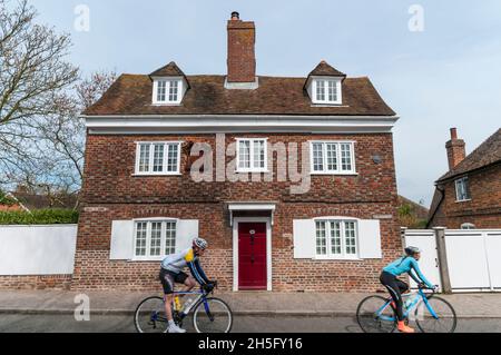 Deux cyclistes (motion floue} passant le 17ème siècle Mill Farmhouse dans la rue, Cobham, Kent. Banque D'Images