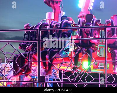 Les enfants se sont empais de leurs sièges avec leurs jambes pendantes en dessous; prêts à partir pour leur tour de parc d'expositions Vortex tournoyant, illuminé la nuit. Banque D'Images