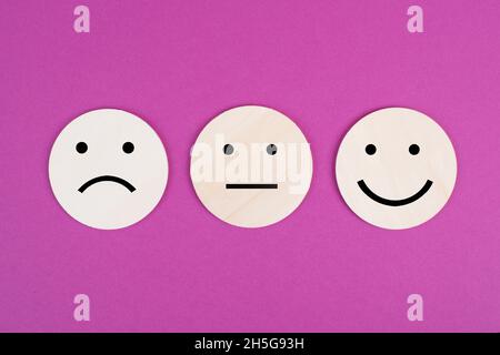 Trois visages, souriant, triste dans différentes couleurs sur fond rose, espace de copie, notation, communication, commentaires des clients Banque D'Images