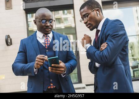Rencontre de deux partenaires hommes d'affaires afro-américains noirs en costumes et en lunettes à l'extérieur Banque D'Images