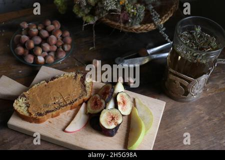 Plateau en bois avec tarte à la crème au chocolat et tranches de figues et de poires juteuses près d'un bol de noisettes Banque D'Images