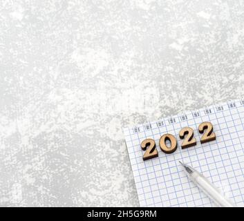 Bloc-notes et stylo sur le gris.Numéros en bois date 2022.Une feuille de papier vierge et un stylo blanc. Banque D'Images