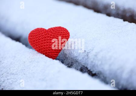 Coeur rouge tricoté dans la neige sur un banc de parc.Carte de Saint-Valentin, symbole de l'amour, fond pour un événement romantique en hiver, fête de Noël Banque D'Images