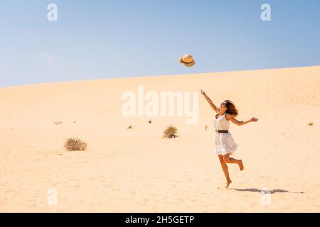 Une jeune femme caucasienne se fait un plaisir de jeter son chapeau dans les dunes du Parc naturel de Corralejo, en Espagne Banque D'Images