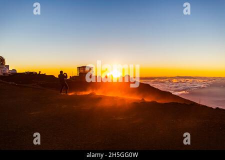 Haleakala Observatory bâtiments au-dessus des nuages avec un coucher de soleil doré et une vue sur l'océan en dessous; Maui, Hawaii, États-Unis d'Amérique Banque D'Images