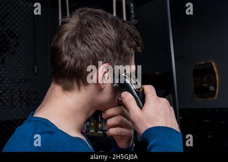 Un gars avec des cheveux foncés coupe ses cheveux sur la tête avec une machine électrique.Soins personnels à domicile. Banque D'Images