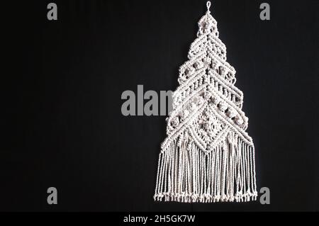 Décoration d'arbre de Noël macrame en fils de coton naturel blanc sur fond noir.Sapin de noël de fête tressé à partir de fils sur fond sombre Banque D'Images