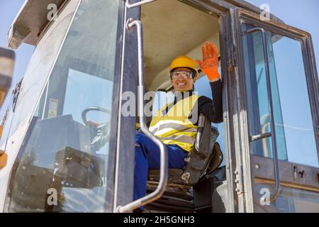 Homme joyeux assis dans le tracteur et faisant un geste bonjour Banque D'Images