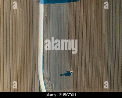 Vue aérienne d'un tracteur travaillant dans un champ agricole au coucher du soleil près d'Aquileia, Udine, Friuli Venezia Giulia, Italie. Banque D'Images