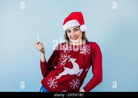 Jeune femme latine tenant une bougie de noël dans un chapeau de noël sur fond bleu au Mexique Amérique latine Banque D'Images