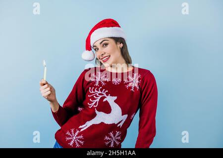 Jeune femme latine tenant une bougie de noël dans un chapeau de noël sur fond bleu au Mexique Amérique latine Banque D'Images