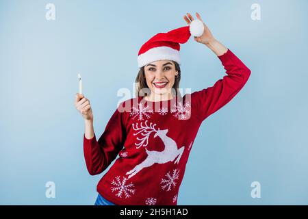 Jeune femme latine tenant une bougie de noël dans un chapeau de noël sur fond bleu au Mexique Amérique latine Banque D'Images