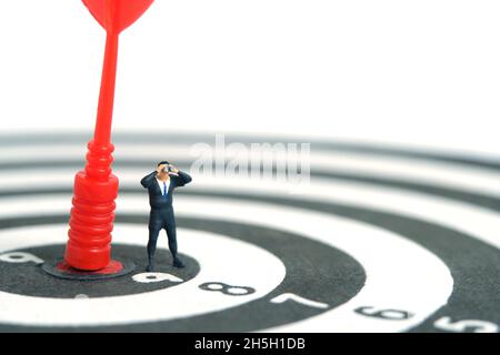 Hommes d'affaires debout au-dessus de la flèche rouge sur le plan de travail à l'aide de jumelles. Photo miniature de jouets de personnes minuscules. Isolé sur fond blanc. Banque D'Images