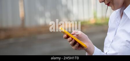 Photo en gros plan des mains d'une femme touchant l'écran d'un téléphone mobile moderne tout en se tenant sur un arrière-plan de rue flou.Hipster fille est en train de taper e Banque D'Images