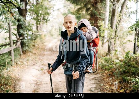 Homme randonnée avec un enfant endormi dans la montagne.Enfant assis dans un sac à dos sur le dos du père.Aventure familiale active en forêt avec une fille fatiguée.Froid Banque D'Images