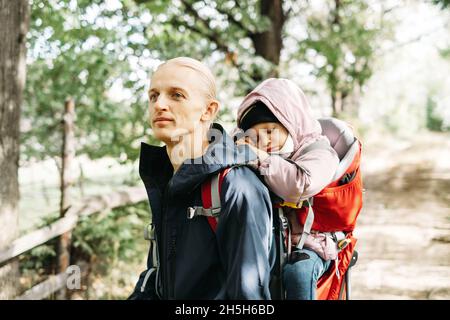 Homme randonnée avec un enfant endormi dans la montagne.Enfant assis dans un sac à dos sur le dos du père.Aventure familiale active en forêt avec une fille fatiguée.Froid Banque D'Images