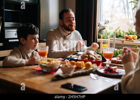 Vue latérale d'une jeune famille heureuse appréciant à table de Noël festive pendant la fête de famille de vacances. Banque D'Images