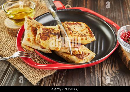 Crêpes à la viande, coupes avec couteau sur plaque sur fond de bois foncé Banque D'Images