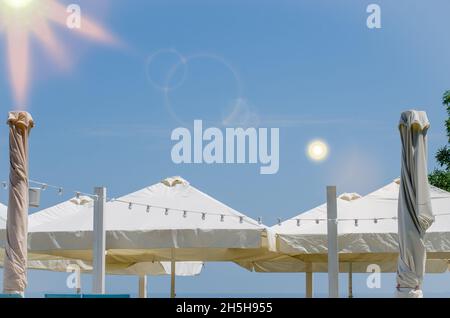 Café extérieur d'été avec grands parasols blancs ouverts et fermés, guirlande blanche et ciel bleu avec espace libre Banque D'Images