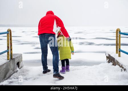 Un enfant avec son père marche à proximité d'un lac ou d'une rivière gelé Banque D'Images