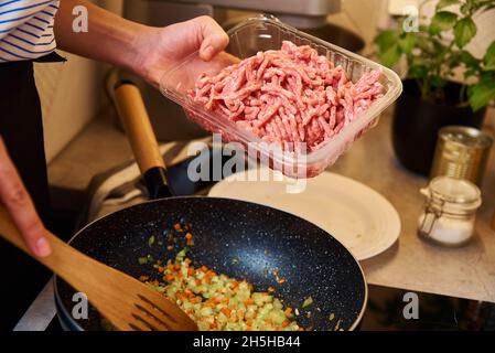 Femme cuisant de la sauce bolognaise dans une poêle à induction dans la cuisine Banque D'Images