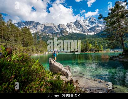 Jeune homme debout sur un rocher, vue sur la distance, lac Eibsee et Zugspitze au printemps avec neige, montagnes Wetterstein, près de Grainau, Upper Banque D'Images