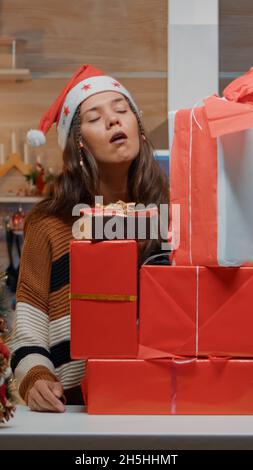 Femme festive mettant des cadeaux sur le comptoir de cuisine dans la cuisine conçue pour la célébration de la veille de noël.Jeune personne gaie préparant des boîtes avec des cadeaux pour les amis et la famille à la maison Banque D'Images