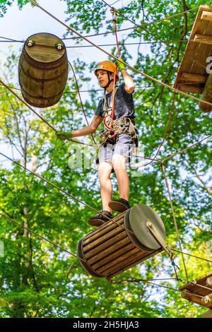 Garçon sur un baril flottant dans la forêt d'escalade et le cours de cordes élevées, Potsdam Adventure Park, Potsdam, Brandebourg, Allemagne Banque D'Images