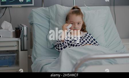 Portrait d'un malade vulnérable seul petit enfant regardant dans la caméra en pleurant pendant l'examen de la maladie dans la salle d'hôpital. Enfant hospitalisé se reposant au lit après avoir subi une chirurgie de récupération Banque D'Images