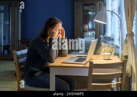 Femme en pull travaillant sur un ordinateur portable dans le salon de la maison.Ressentez le stress, l'anxiété et la fatigue Banque D'Images
