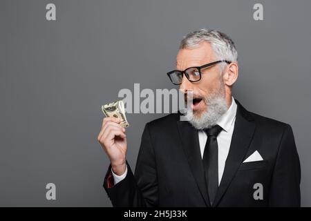 un homme d'affaires d'âge moyen choqué regarde les billets de banque en dollars isolés sur fond gris Banque D'Images