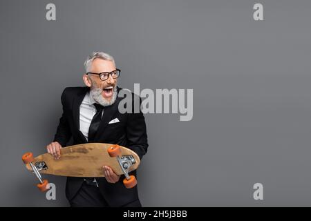 homme d'affaires d'âge moyen en costume et lunettes tenant la planche de bord et criant sur le gris Banque D'Images