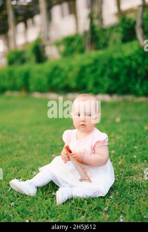 Budva, Monténégro - 17.04.2017: Petite fille mignonne est assise sur l'herbe verte dans le jardin et tient un ventilateur pliant dans ses mains.Villa Milocer, Monténégro Banque D'Images