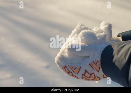 mains tenant une pile de neige étincelante propre, portant des mitaines tricotées blanches, soleil brillant, heap brillant, jour d'hiver ensoleillé, fond neigeux avec des faisceaux lumineux, des stries, des lignes, des cristaux de glace, des flocons de neige Banque D'Images