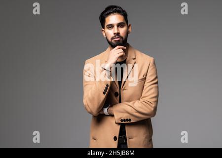 Portrait d'un homme indien beau barbu satisfait et réussi en chemise et gilet debout, tenant son menton isolé sur fond gris Banque D'Images