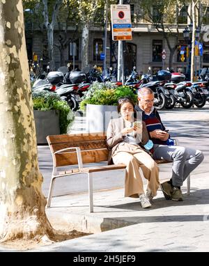 Homme et femme assis sur le banc pour regarder leurs téléphones mobiles, Barcelona Spain Passeig de Gracia Banque D'Images
