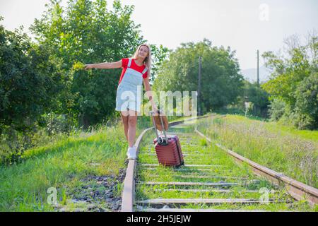 femme contentée avec un chapeau marche sur les rails avec une valise Banque D'Images