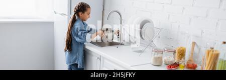 Vue latérale de l'enfant versant de l'eau dans une casserole près de la nourriture dans la cuisine, bannière Banque D'Images