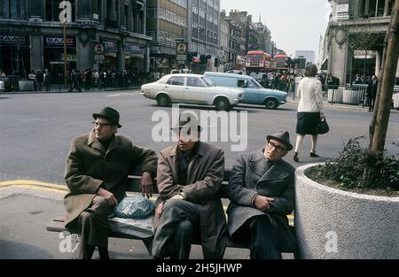 Londres 1982.Vue sur la rue d'Oxford Circus avec trois hommes en manteaux assis sur un banc.Crédit Roland Palm. Banque D'Images