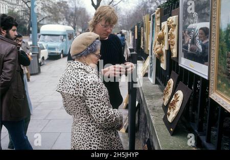 Londres 1982.Une vue d'une rue de Londres avec une dame âgée qui regarde l'art pendu sur la clôture à un parc.Crédit Roland Palm. Banque D'Images