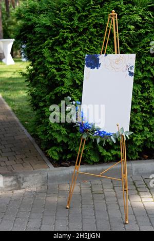 Tableau de mariage, maquette, chevalet d'invitation, avec espace pour une inscription, décoré de fleurs fraîches.Décoration festive, espace pour le photocopie.Mise au point sélective douce. Banque D'Images