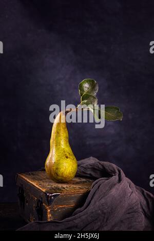 Vie rurale encore, photographie sombre à touches peu importantes - vue d'une poire de conférence solitaire sur une ancienne boîte en bois, gros plan avec une mise au point sélective Banque D'Images