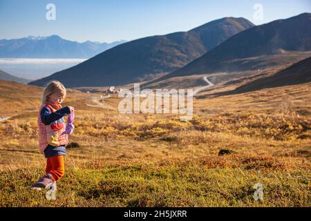 Une jeune fille caucasienne portant un gilet multicolore marche sur la toundra lors d'une sortie vers l'aire de loisirs d'État de Hatcher Pass, Hatcher Pass Lodge... Banque D'Images