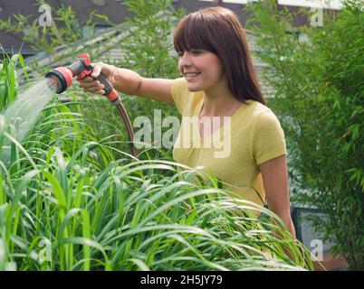 Jeune femme arrosoir des plantes avec tuyau de jardin sur la terrasse dans son jardin; Allemagne Banque D'Images