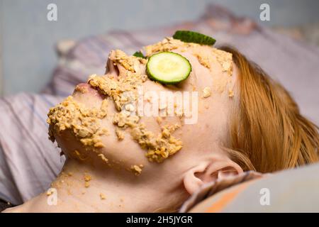 Une femme fait un masque cosmétique à la maison à partir de flocons d'avoine sur son visage et concombre.Traitements anti-âge, concept de soins de la peau. Banque D'Images