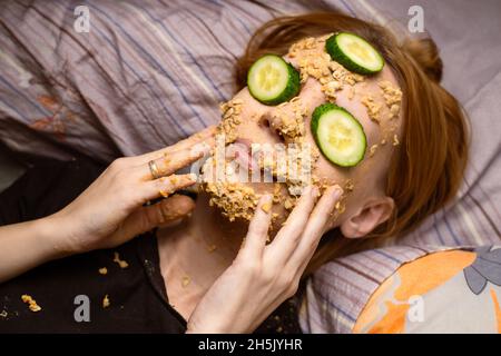 Une femme fait un masque cosmétique à la maison à partir de flocons d'avoine sur son visage et concombre.Traitements anti-âge, concept de soins de la peau. Banque D'Images