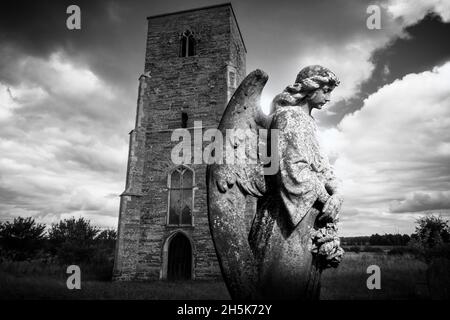 Image d'un ange sculpté, tête de pierre devant une église dans un cimetière avec un ciel noir et blanc spectaculaire. Banque D'Images