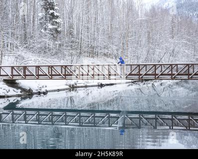 Garçon jouant avec la neige en marchant sur une passerelle à Knik River le long de Old Glenn Highway en hiver; Palmer, Alaska, États-Unis d'Amérique Banque D'Images