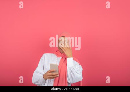 jeune femme musulmane africaine souriant tout en utilisant son téléphone isolé sur fond rose Banque D'Images