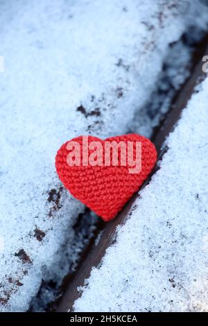 Coeur rouge tricoté dans la neige sur un banc, plan vertical.Carte de Saint-Valentin, symbole de l'amour, fond pour un événement romantique en hiver, Noël Banque D'Images